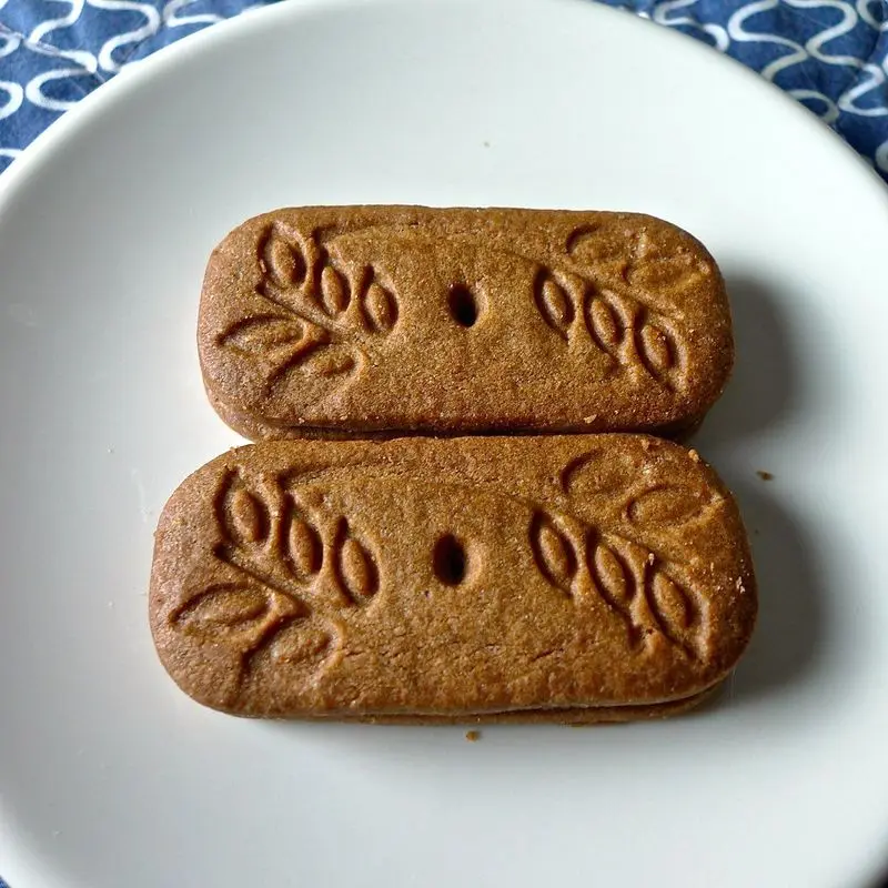 Dos galletas de canela caramelizada con relieve de hojas sobre un plato blanco