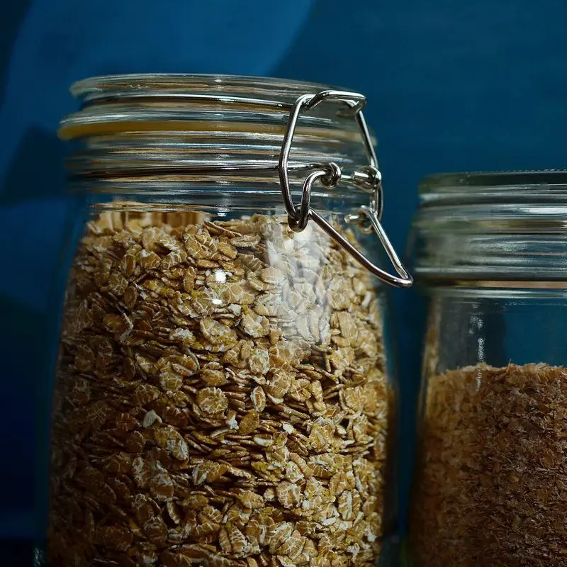 Dos tarros de cristal con copos de espelta y cereales sobre fondo azul