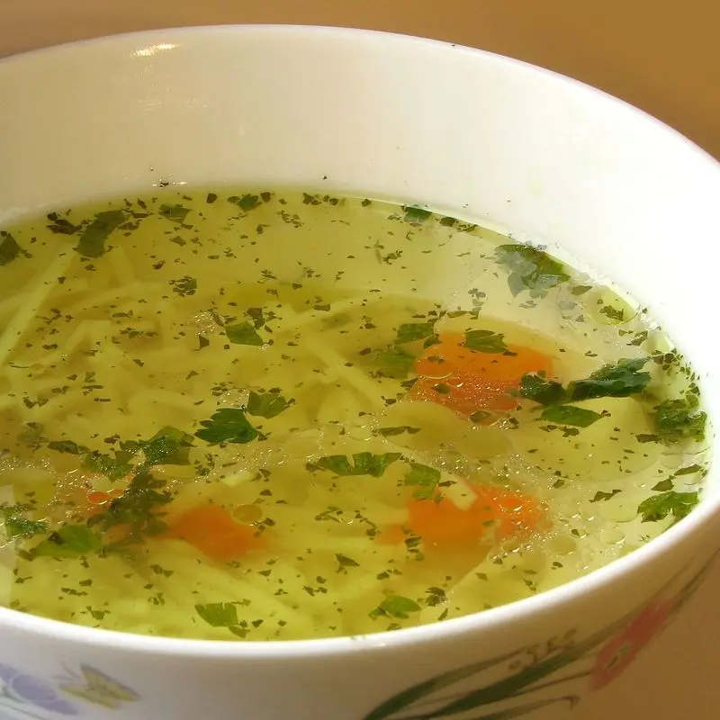 Cuenco blanco con caldo claro, fideos finos y zanahoria