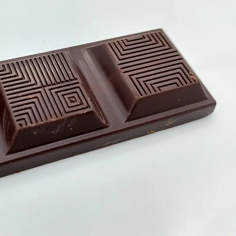 Tableta de chocolate negro sin envoltorio con relieve geométrico sobre fondo blanco
