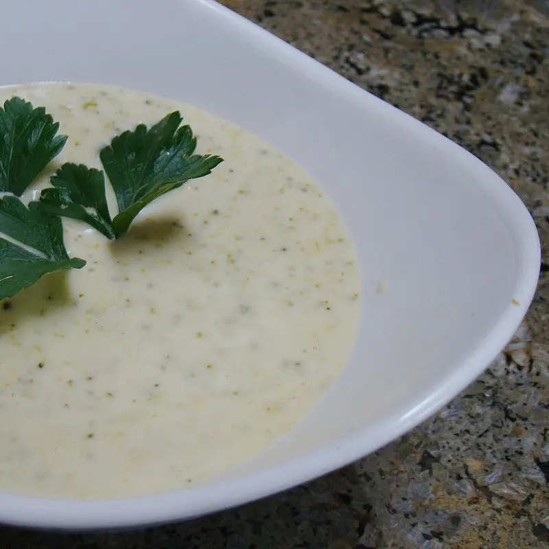Plato hondo blanco con crema de verduras verde y una hoja de perejil