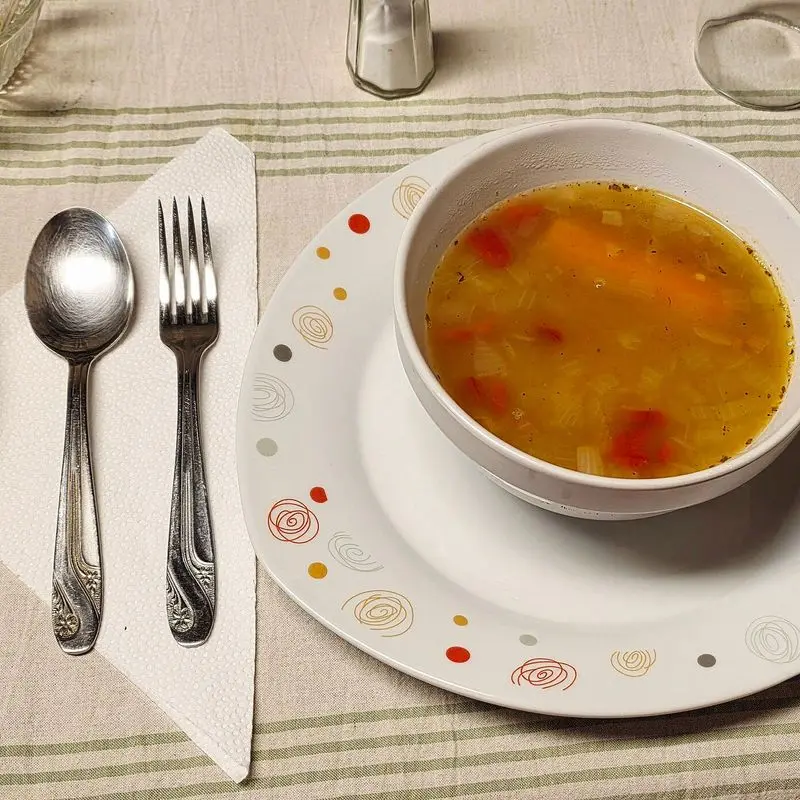 Cuenco blanco con sopa de verduras caliente sobre un plato con cubiertos