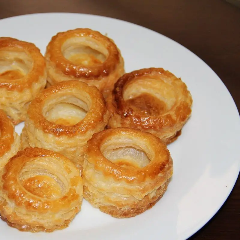 Seis volovanes de hojaldre vacíos y dorados sobre un plato blanco