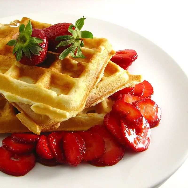 Gofres dorados apilados con fresas y hojas de menta sobre un plato blanco