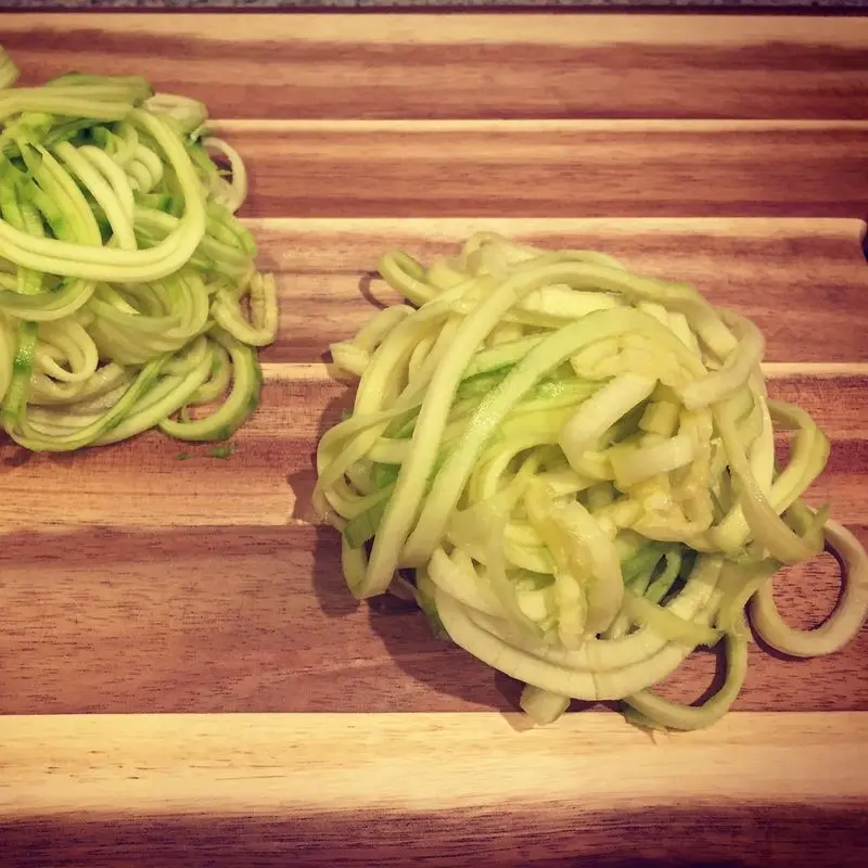 Dos nidos de espaguetis de calabacín crudos sobre una tabla de madera