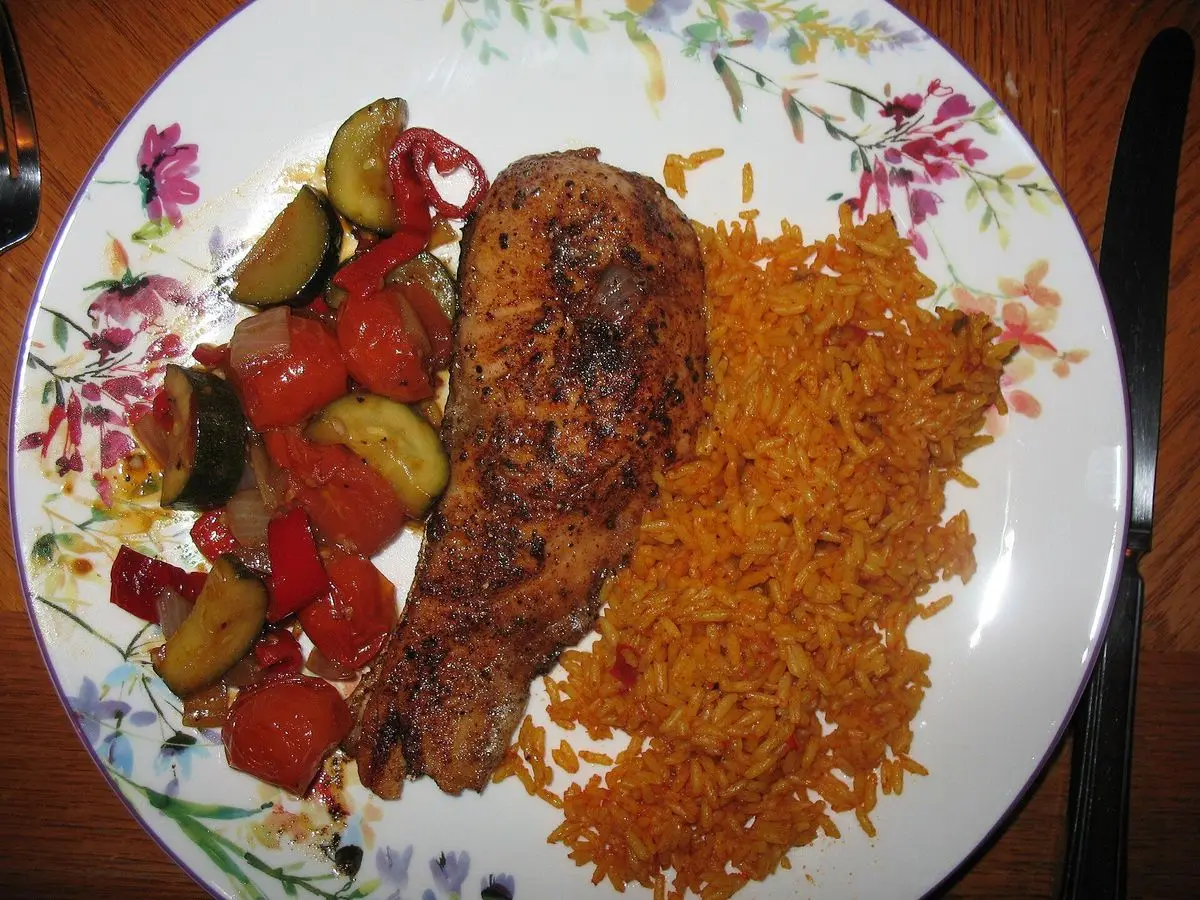 Filete de pescado especiado a la parrilla con arroz sazonado y verduras asadas en un plato floreado
