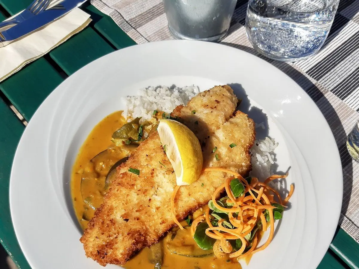 Filete de pescado rebozado sobre arroz con salsa espesa de verduras y una cuña de limón en un plato blanco