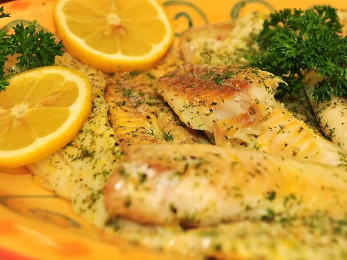 Filetes de pescado blanco con hierbas, rodajas de limón y perejil sobre un plato amarillo