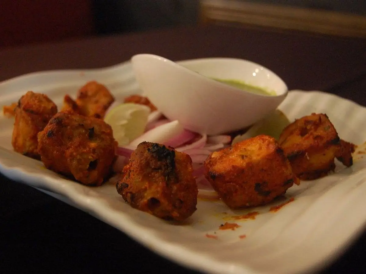 Trozos de pescado asados al estilo tandoori con salsa verde de yogur y cebolla en un plato