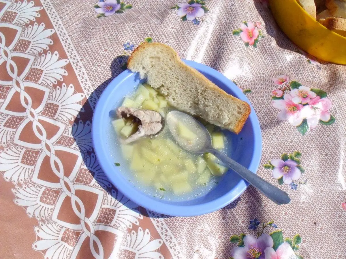 Cuenco azul de sopa de pescado con patatas y una rebanada de pan, sobre un mantel de flores