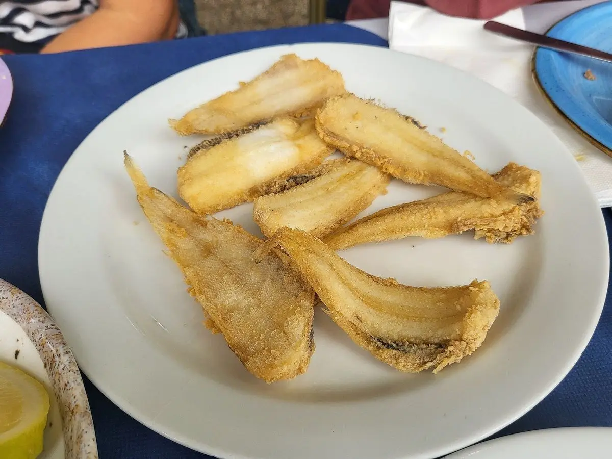 Plato blanco con acedías fritas enharinadas y doradas sobre un mantel azul