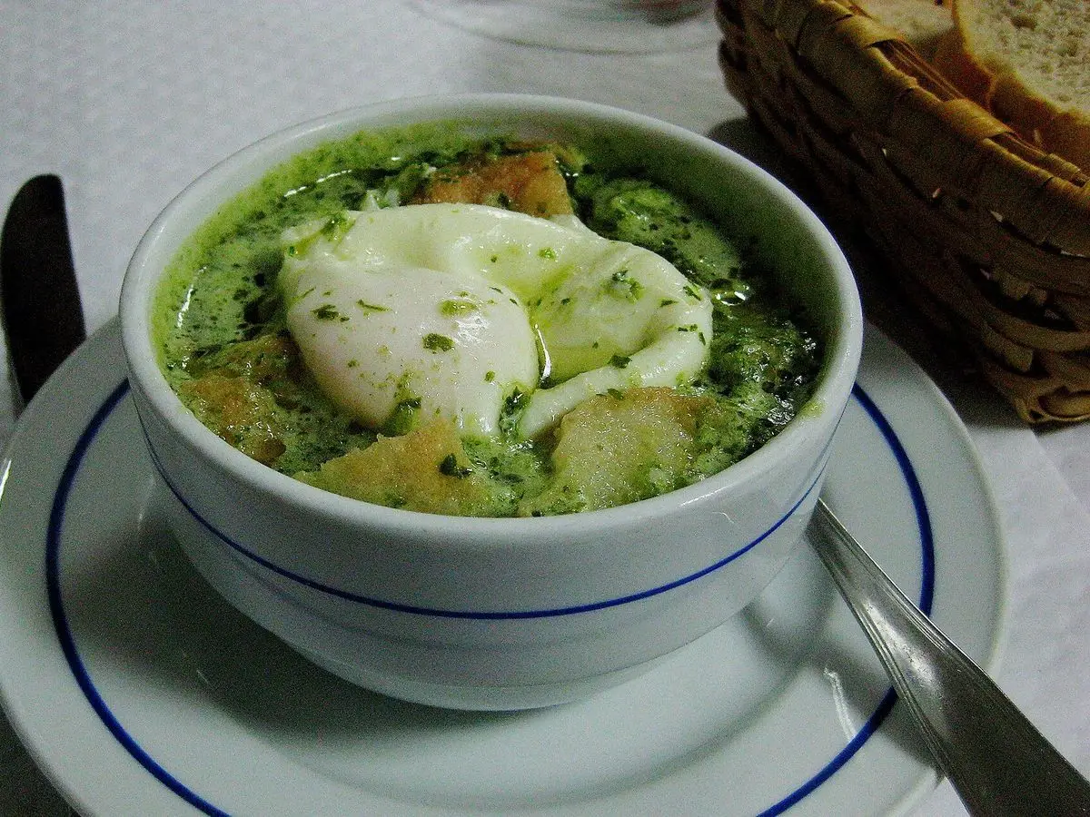 Cuenco de açorda verde de pan con cilantro y un huevo escalfado sobre un plato con filete azul