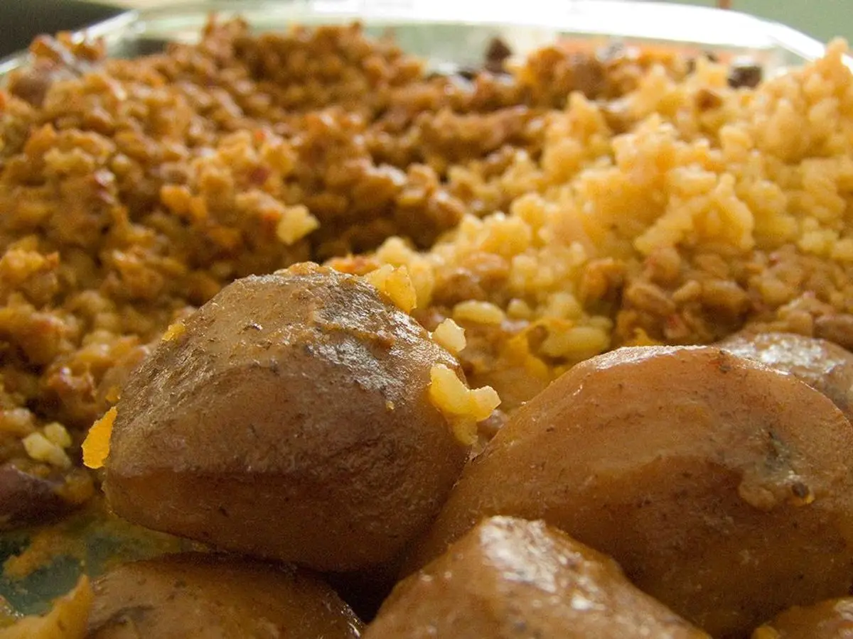 Primer plano de un guiso sefardí con patatas enteras tostadas, trigo y carne desmenuzada