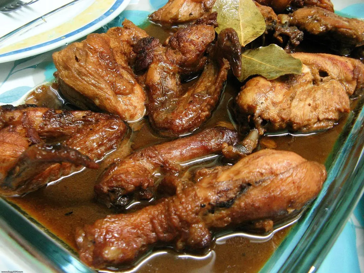 Muslos de pollo guisados en salsa oscura de adobo con laurel en una fuente de cristal