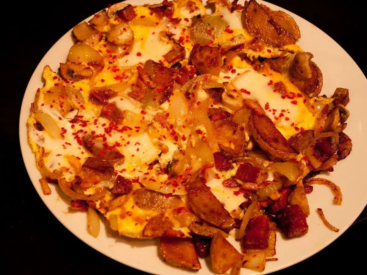 Tortilla de huevo con trocitos de bacon y tomate en un plato blanco