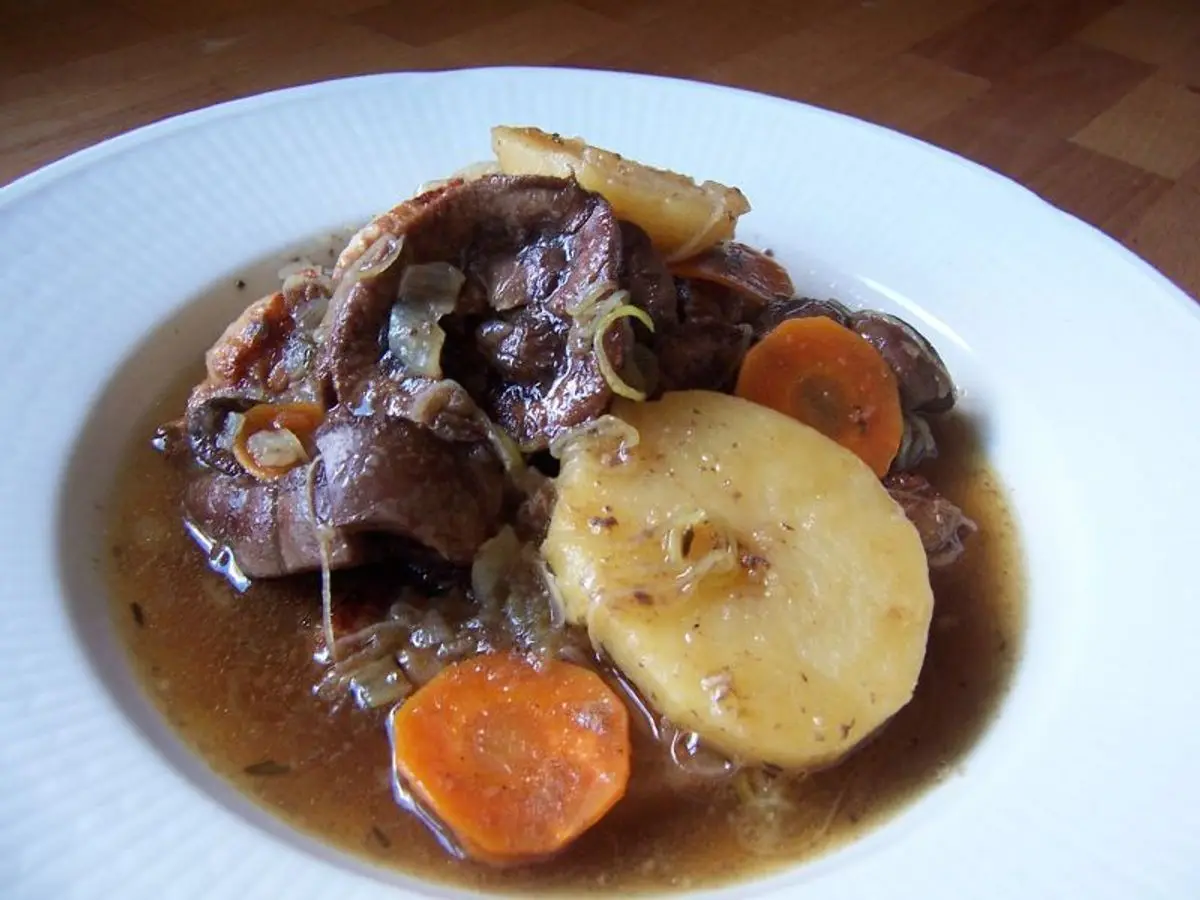 Plato blanco con guiso de carne de cerdo en salsa oscura con rodaja de patata y zanahoria