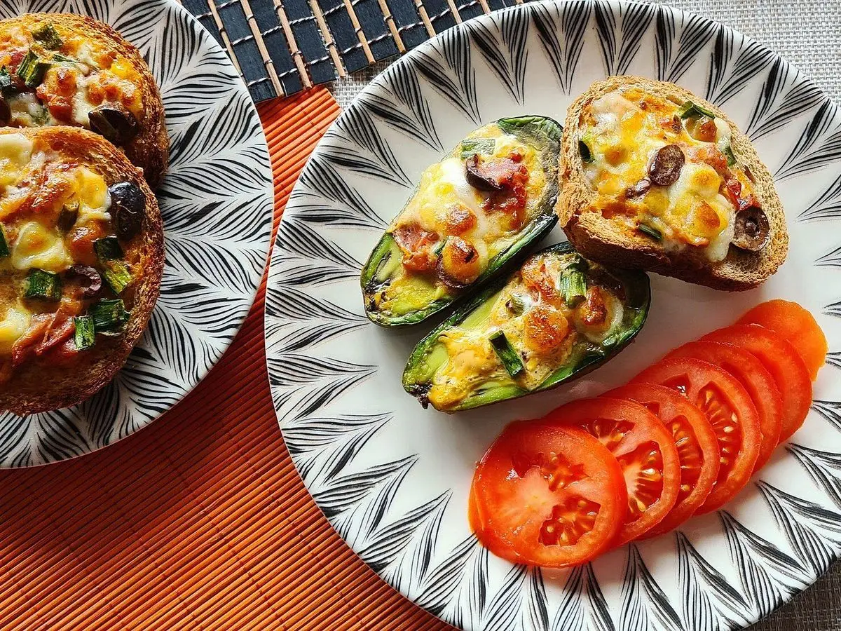 Mitades de aguacate al horno rellenas de huevo gratinado con rodajas de tomate en un plato blanco