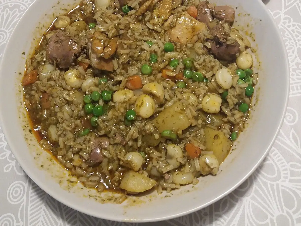 Plato hondo de aguadito peruano verde con arroz, pollo, guisantes y rodajas de lima