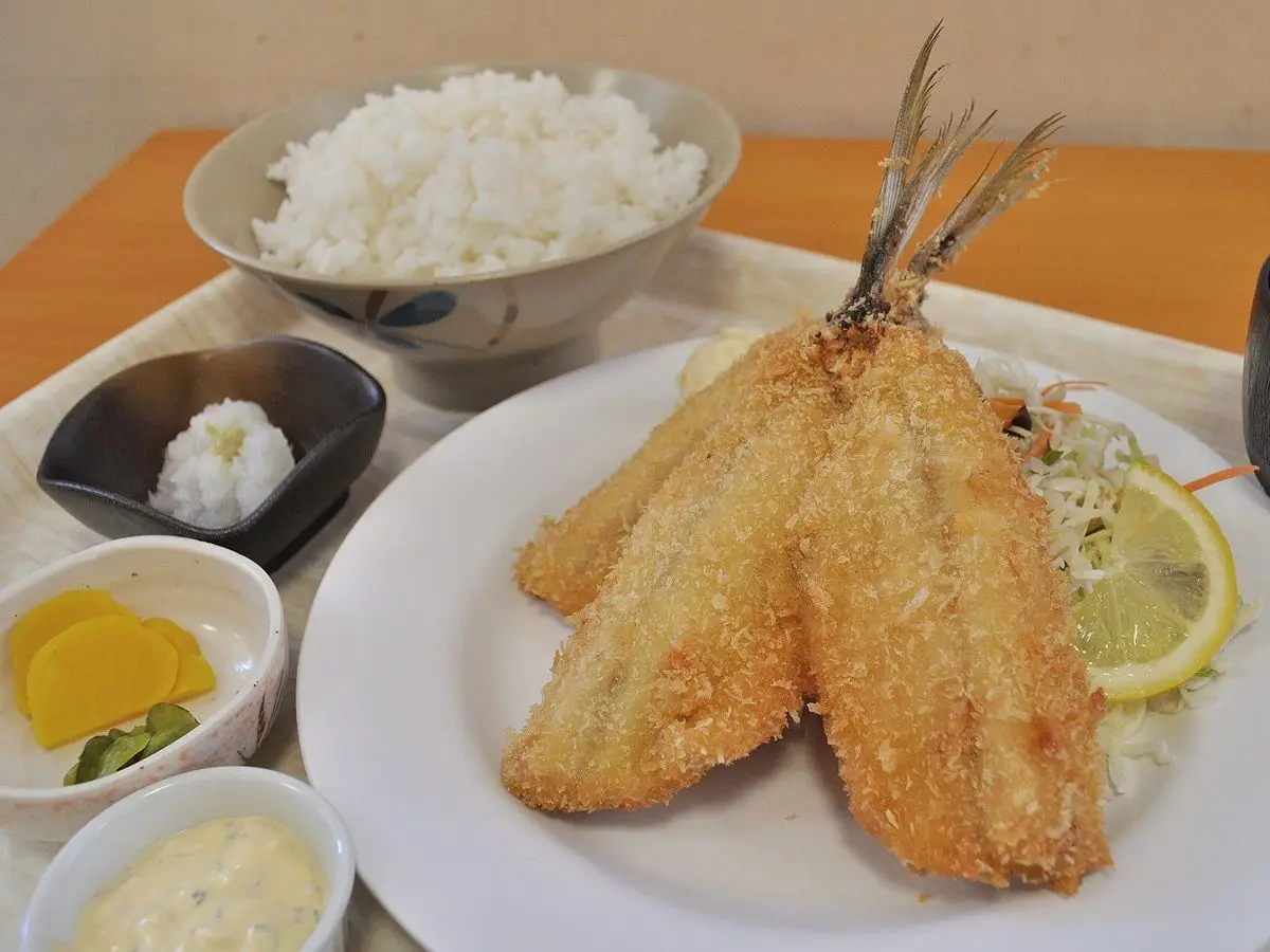Jureles empanados y fritos con limón y col cortada, junto a un cuenco de arroz blanco