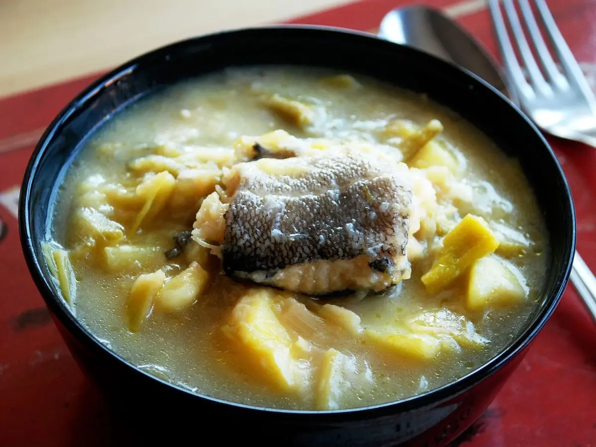 Cuenco negro con guiso caldoso de patata y puerro coronado con un trozo de bacalao