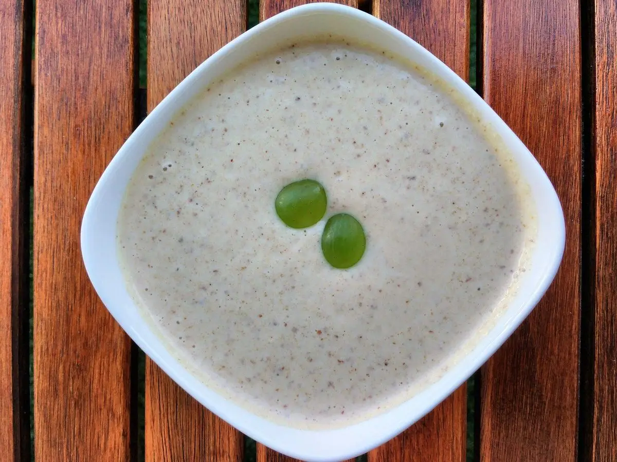 Cuenco blanco de ajoblanco cremoso con dos uvas verdes encima sobre mesa de madera