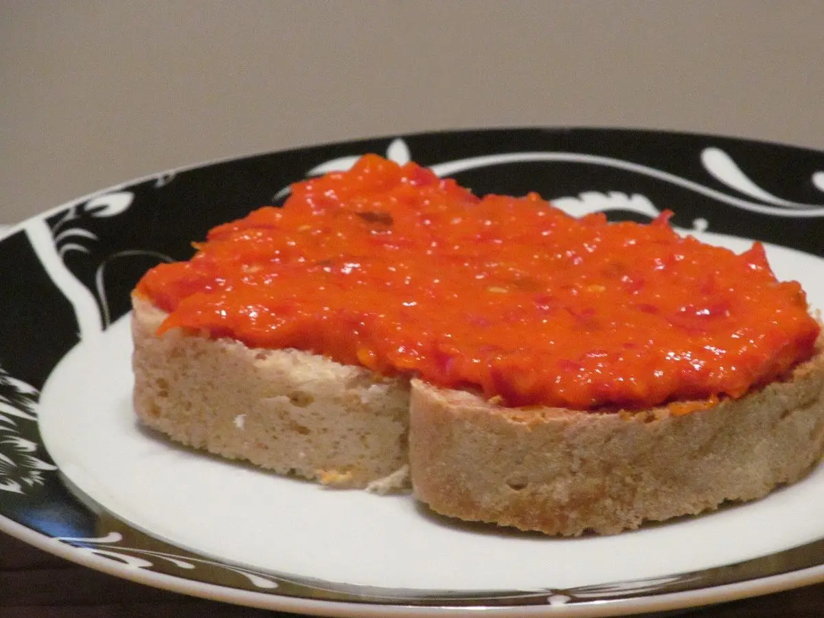 Rebanada de pan untada con ajvar, crema de pimiento rojo asado, sobre un plato blanco y negro