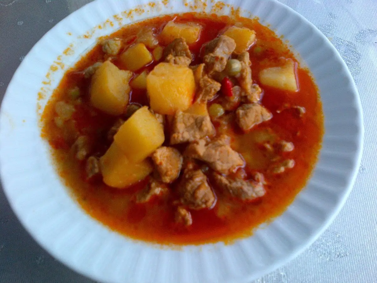 Plato hondo blanco con guiso de carne y patatas en salsa de tomate