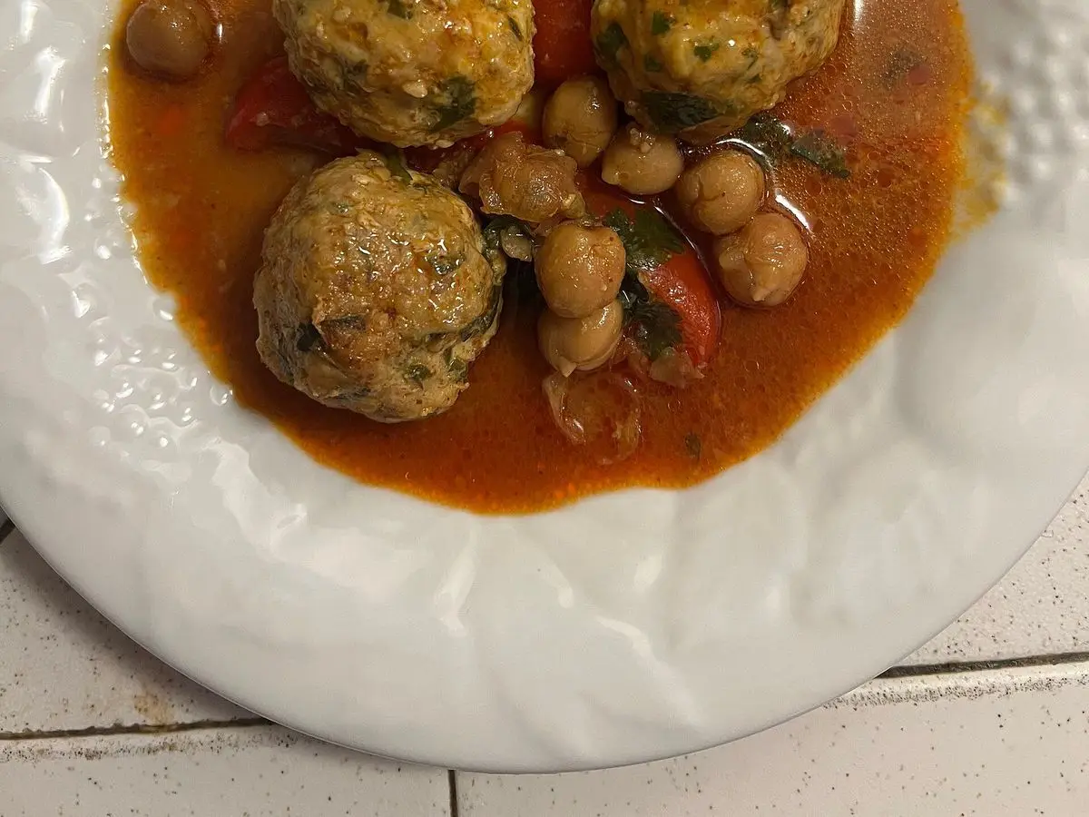Albóndigas de pescado con hierbas en salsa anaranjada con garbanzos y pimiento en un plato blanco