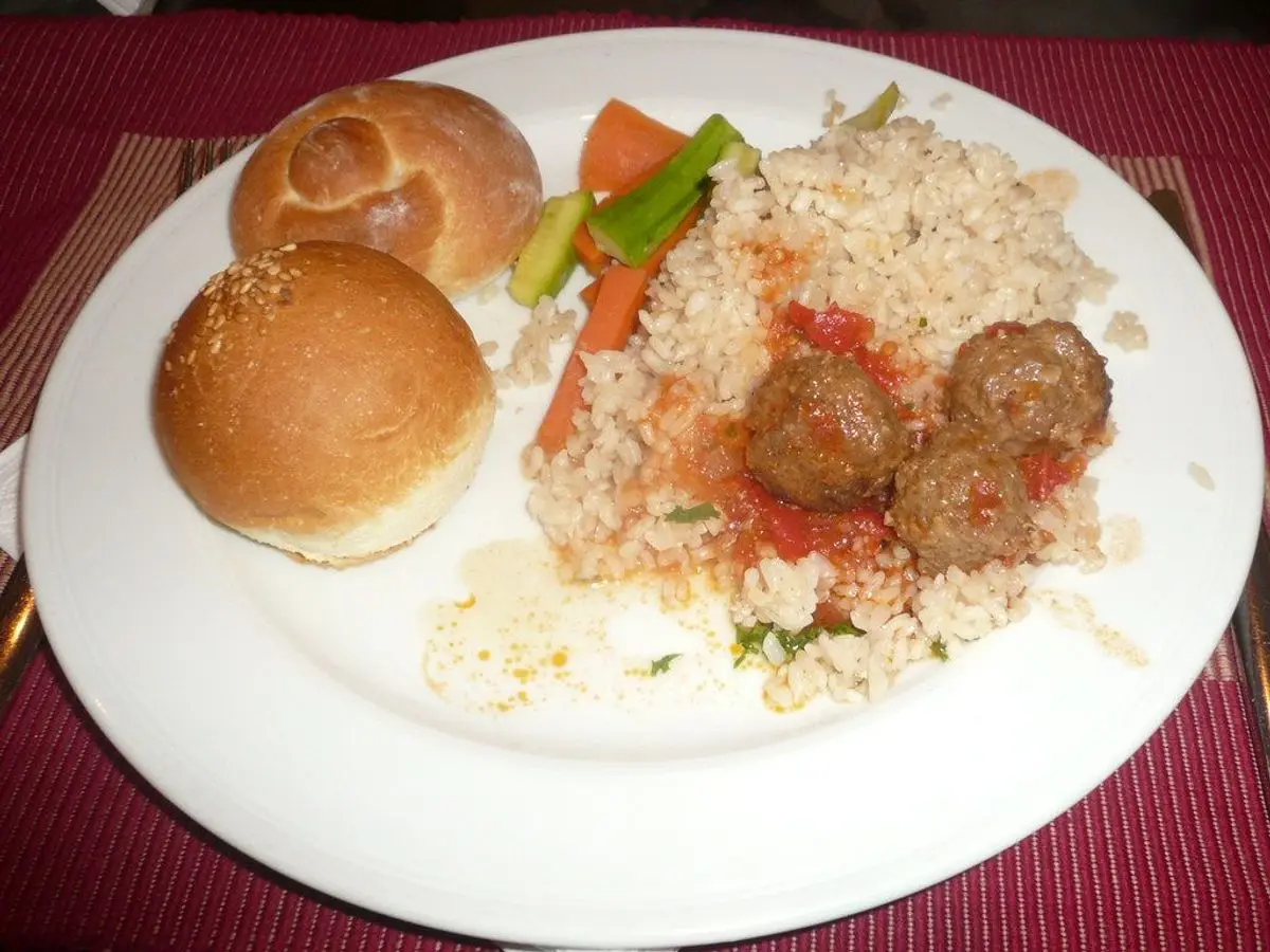 Albóndigas con arroz y zanahoria en un plato blanco junto a dos panecillos