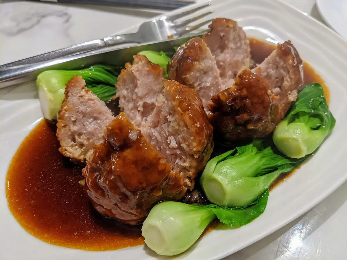 Grandes albóndigas de cerdo cortadas con salsa marrón y pak choi en un plato blanco