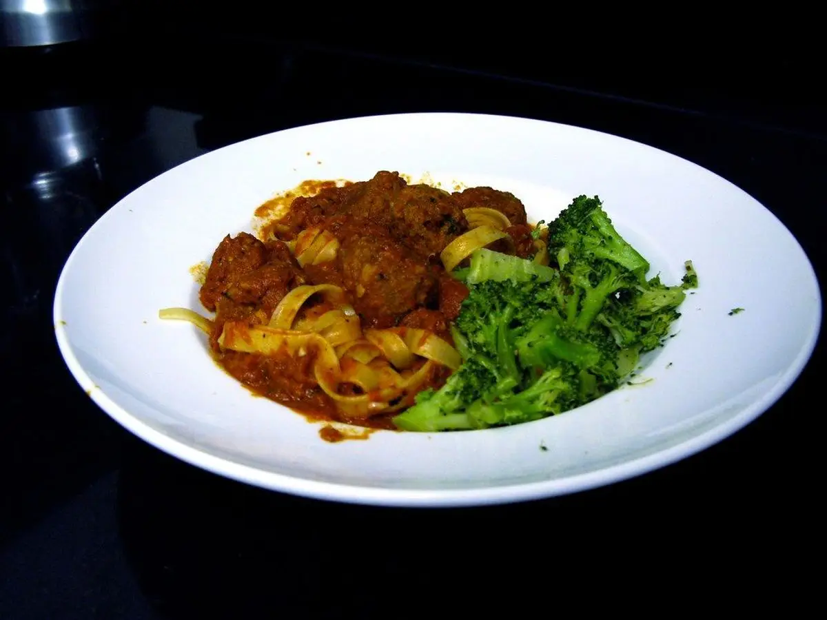 Plato blanco con albóndigas en salsa de tomate, cintas de pasta y brócoli