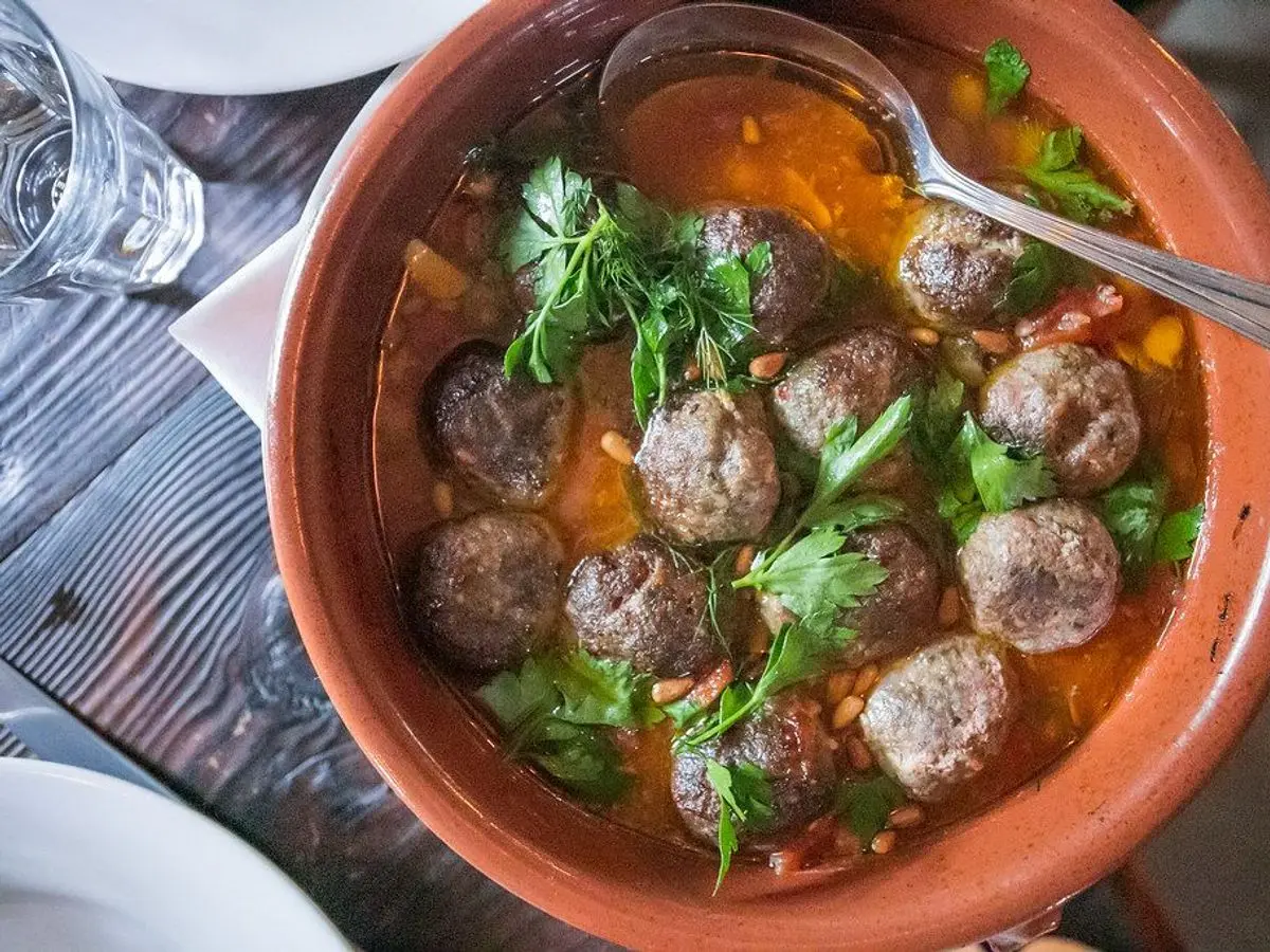 Cazuela de barro con albóndigas en salsa anaranjada y perejil fresco con una cuchara