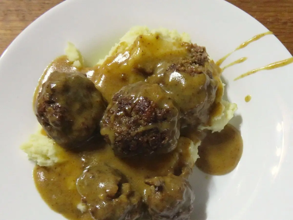 Albóndigas con salsa marrón sobre puré de patata en un plato blanco