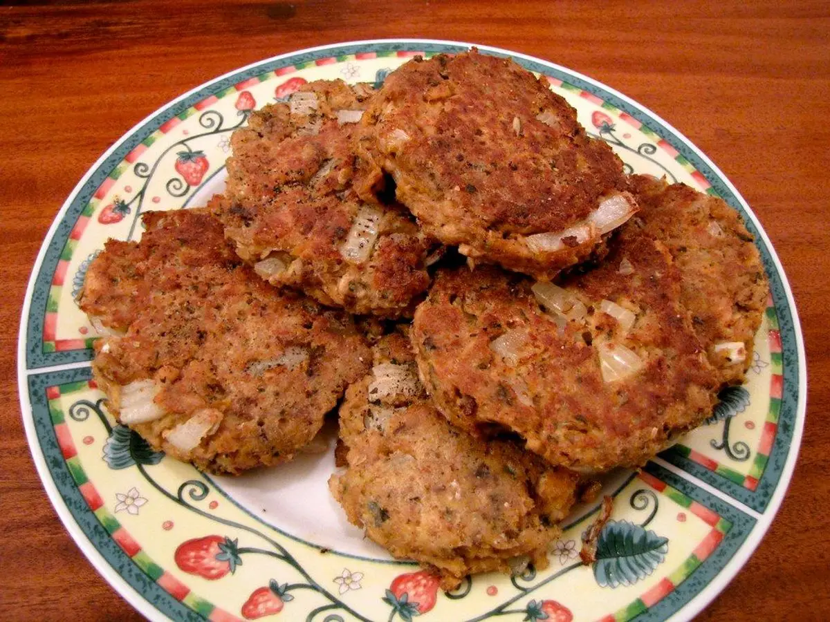 Tortitas de pescado doradas amontonadas en un plato con decoración de fresas