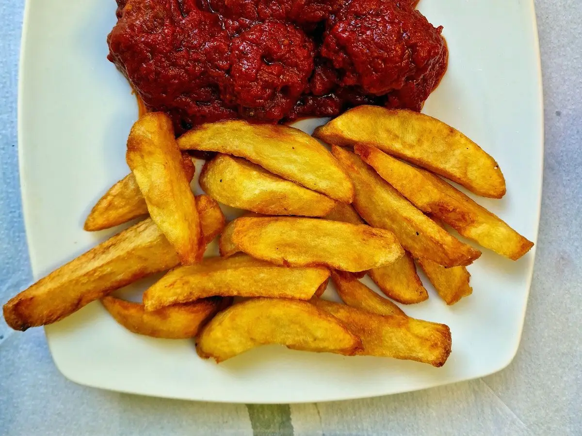 Albóndigas en salsa roja de tomate con patatas fritas en gajos sobre un plato ovalado blanco