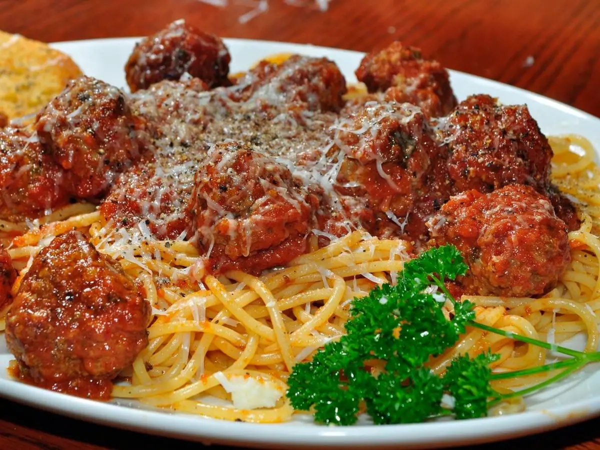 Fuente de albóndigas de carne en salsa de tomate sobre espaguetis, con queso rallado y perejil