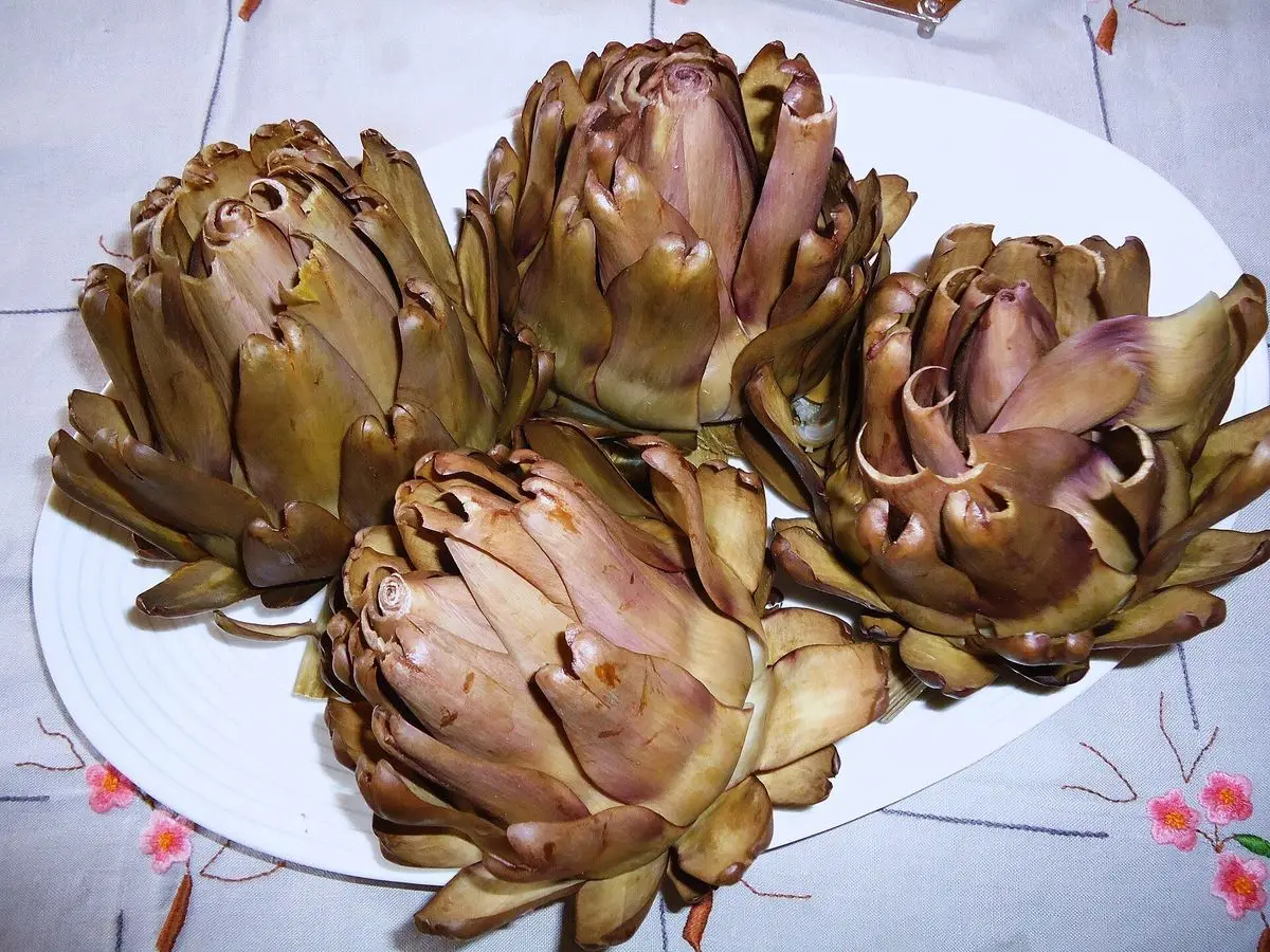 Alcachofas cocidas servidas sobre un plato blanco con mantel de flores
