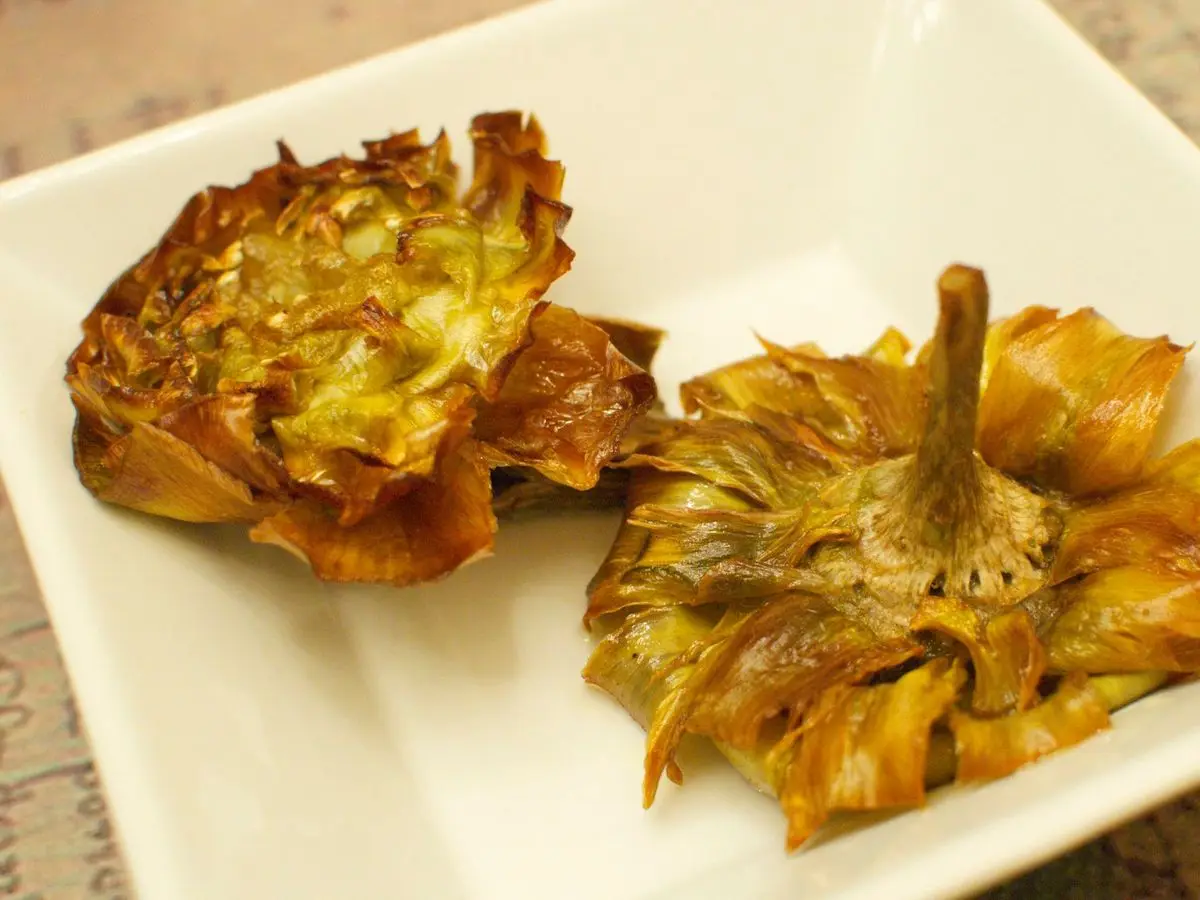 Dos alcachofas fritas doradas y crujientes abiertas como flores sobre un plato blanco