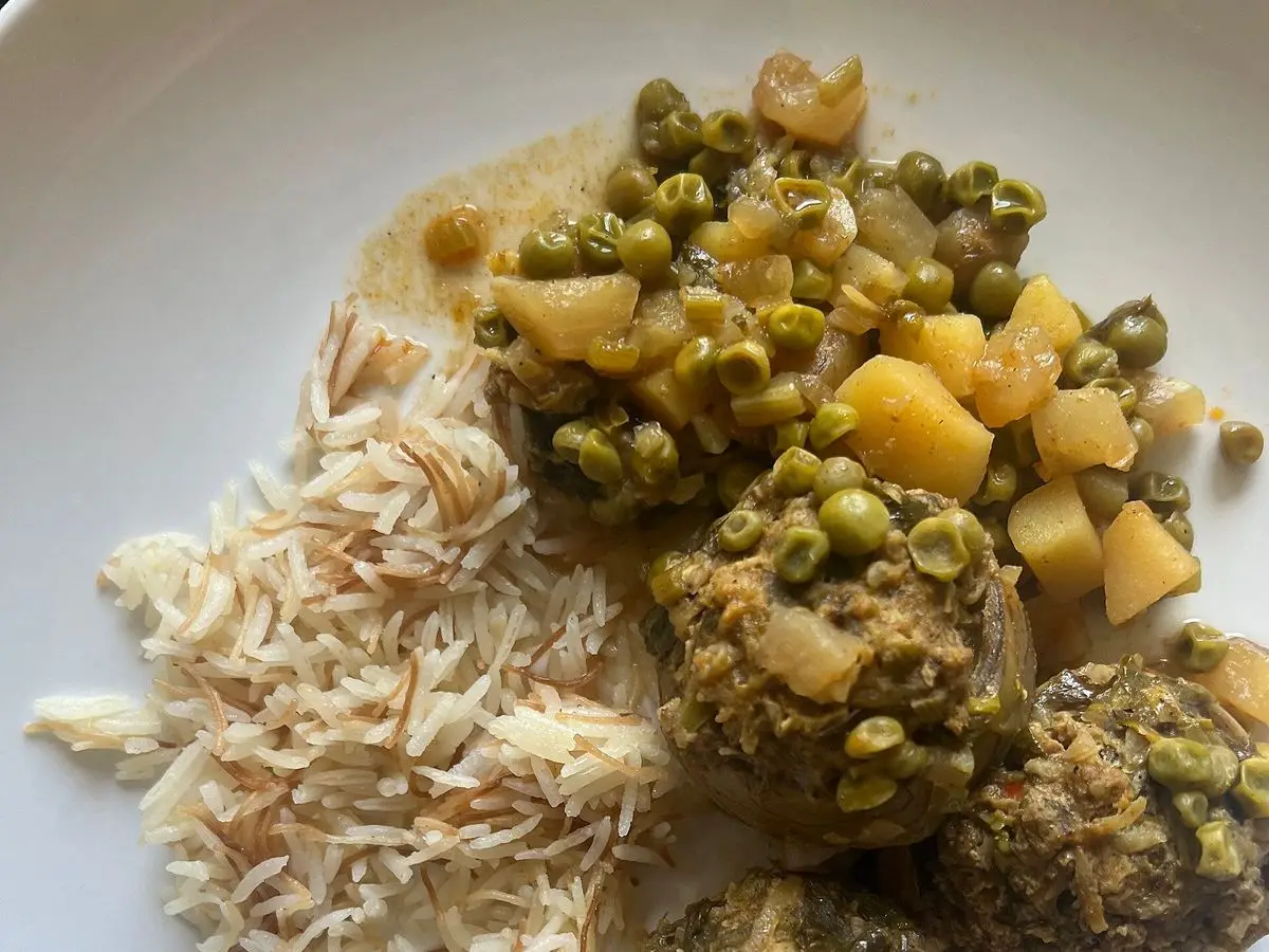 Alcachofas rellenas guisadas con guisantes y patata junto a arroz con fideos en un plato blanco