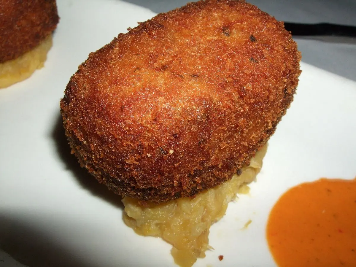 Alcapurria frita y dorada sobre un plato blanco con una salsa anaranjada al lado