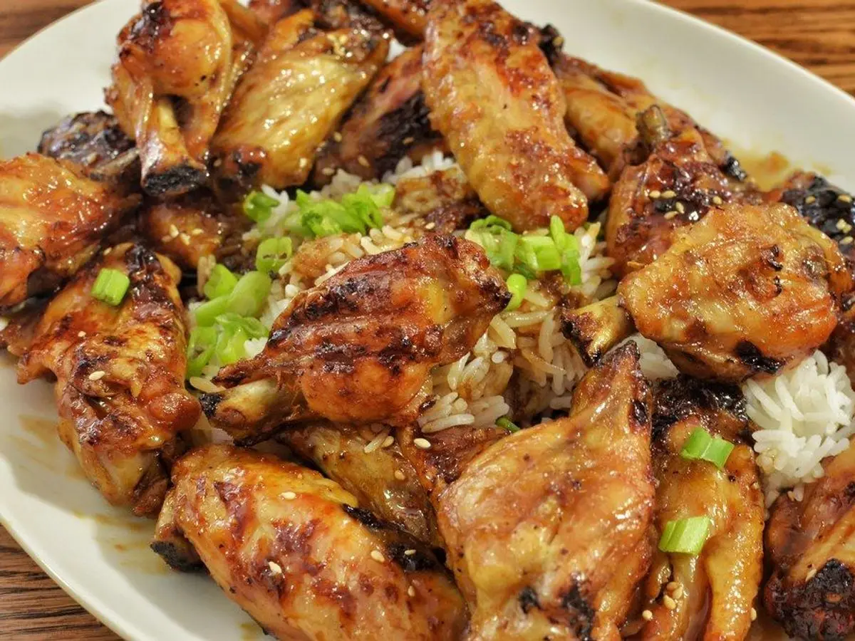 Alitas de pollo asadas con cebolleta picada sobre un plato blanco con arroz