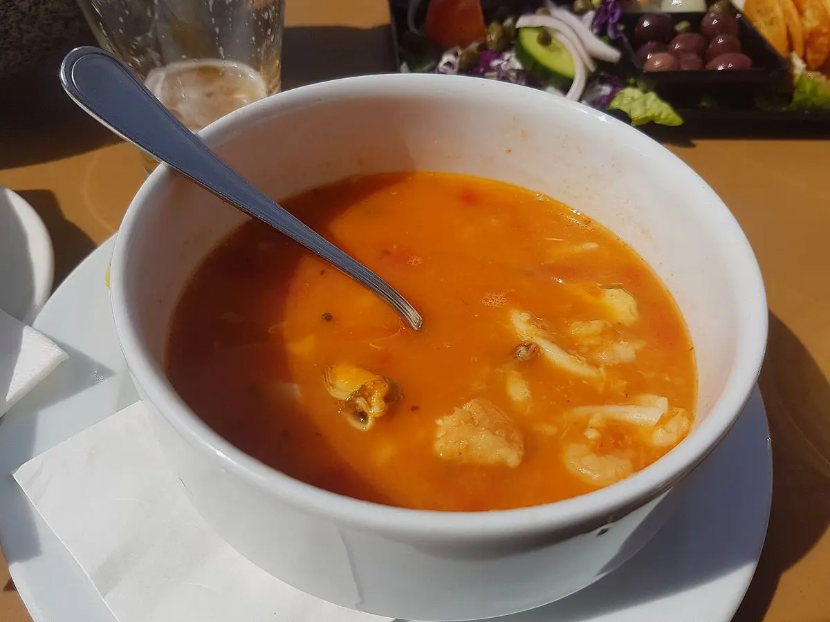 Cuenco blanco de sopa de pescado anaranjada de tomate con trozos de pescado y una cuchara