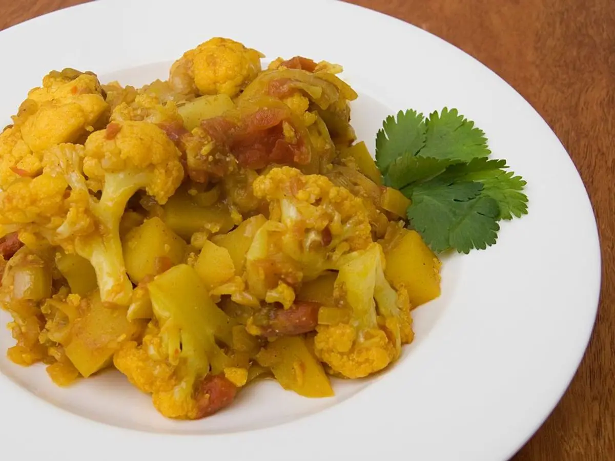 Plato blanco con coliflor y patata especiadas de color amarillo, decorado con cilantro