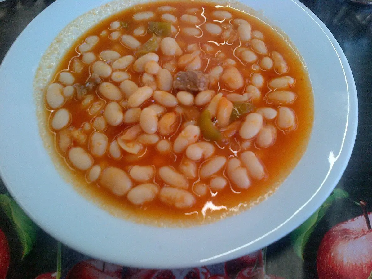 Plato hondo azul de alubias blancas con salsa de tomate y trozos de pimiento