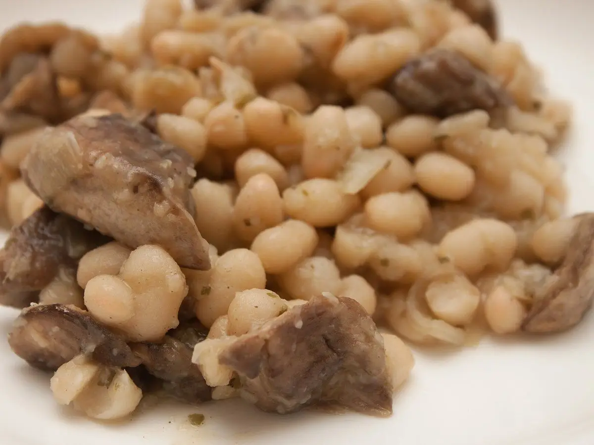 Primer plano de alubias blancas con setas laminadas sobre un plato blanco