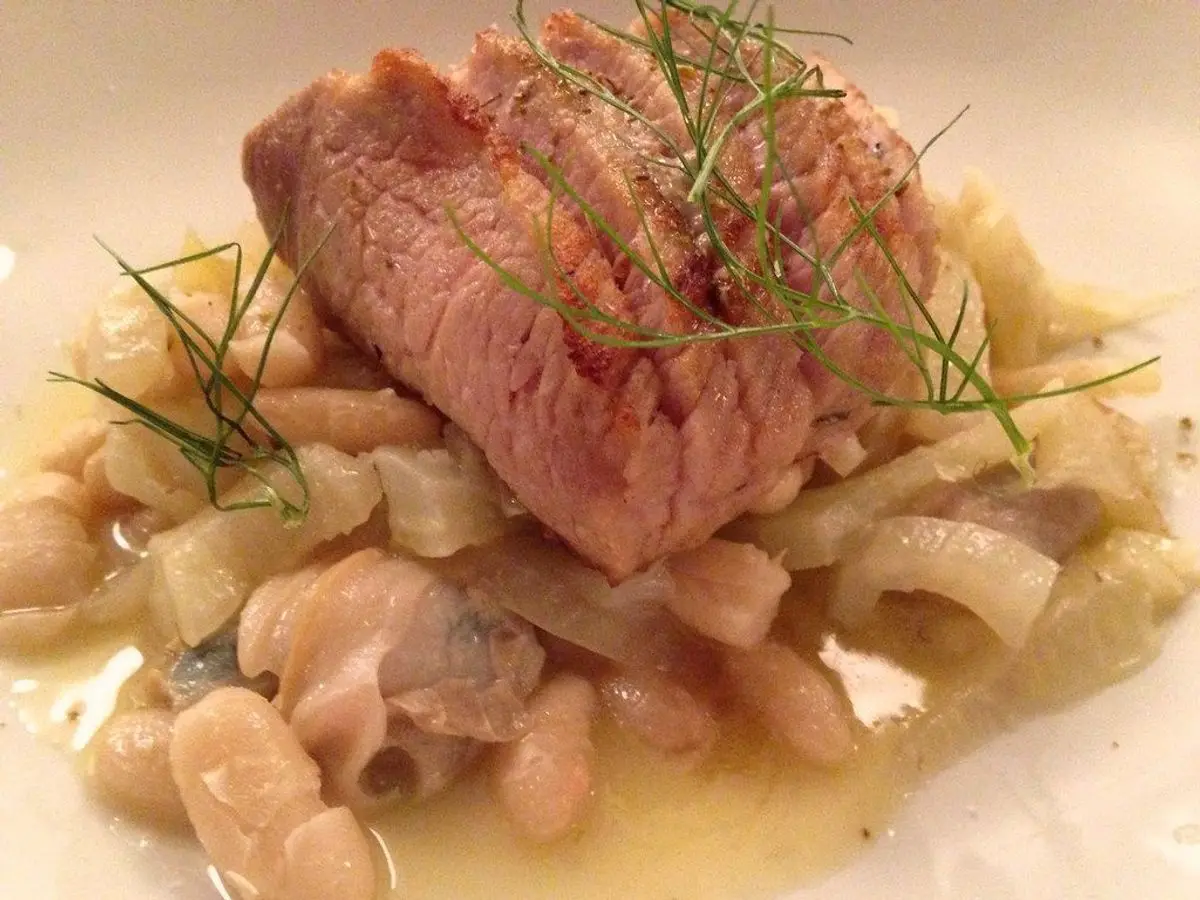 Lomo de pescado sobre alubias blancas con hierbas en un plato blanco