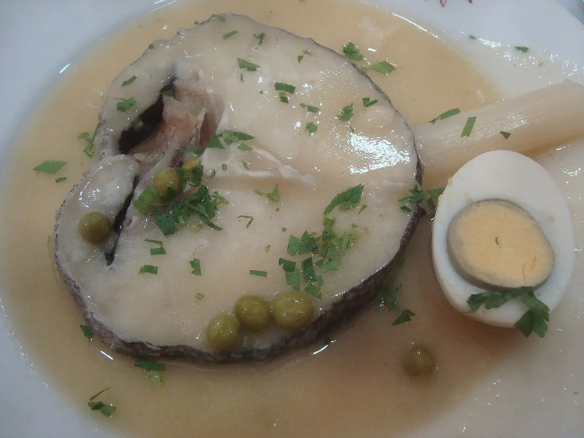 Plato hondo con rodaja de merluza en salsa clara con perejil, guisantes y medio huevo duro