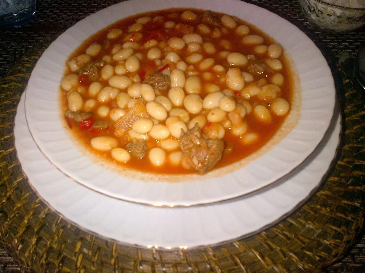 Plato de alubias blancas guisadas con trozos de carne en salsa de tomate sobre un plato blanco