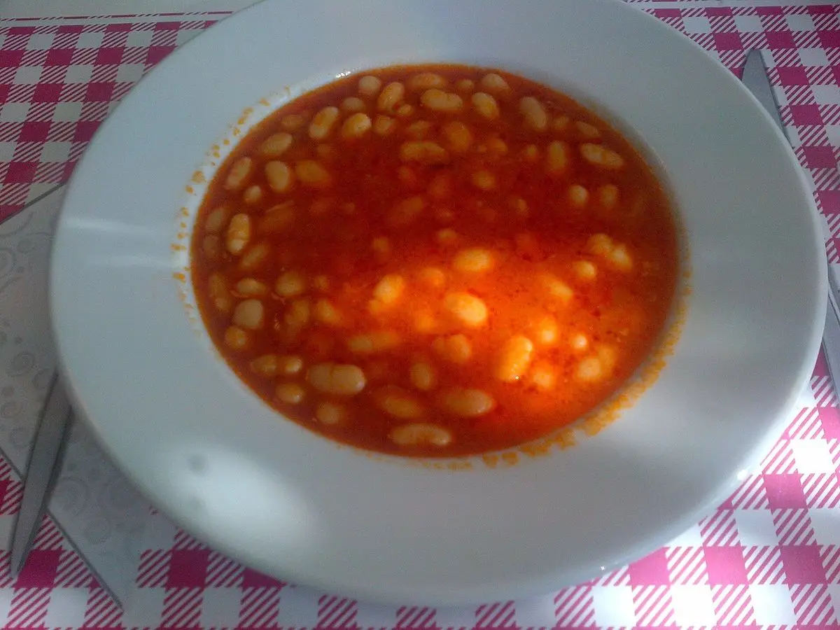 Plato hondo de alubias blancas guisadas en salsa de tomate sobre mantel de cuadros