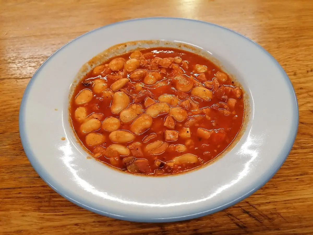 Plato hondo de alubias blancas en salsa de tomate sobre una mesa de madera